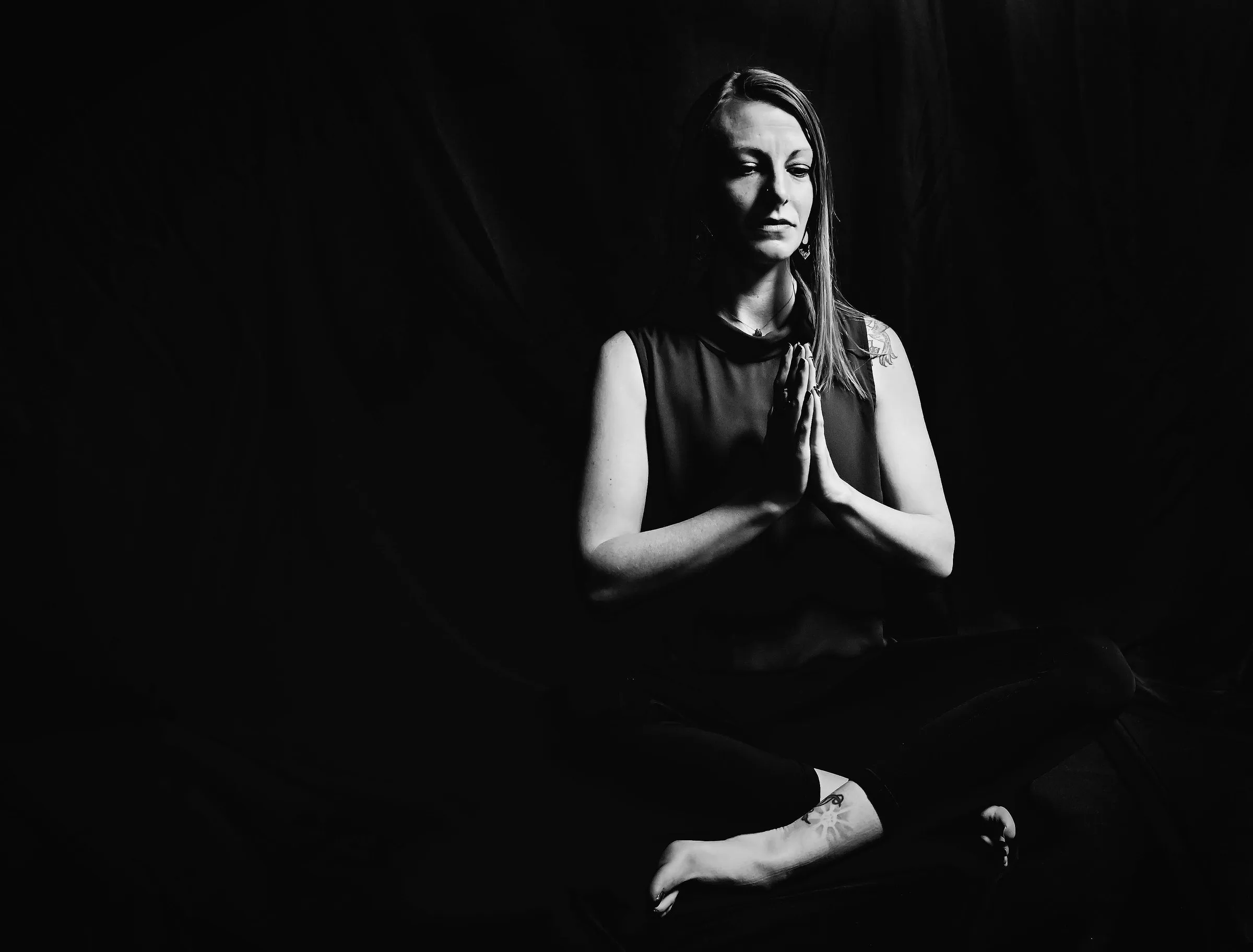 Cora seated in meditation, hands at heart center, in black and white