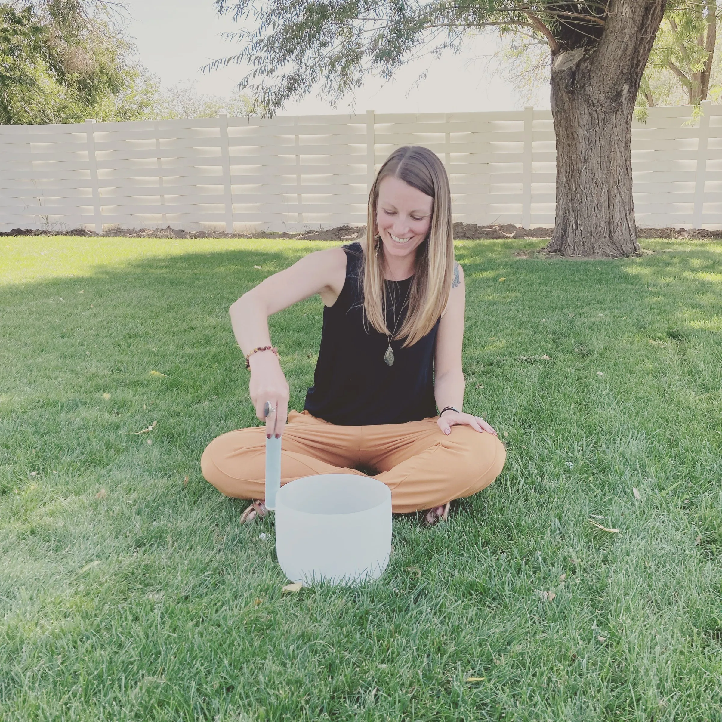 Cora playing a crystal singing bowl on the lawn under a big tree