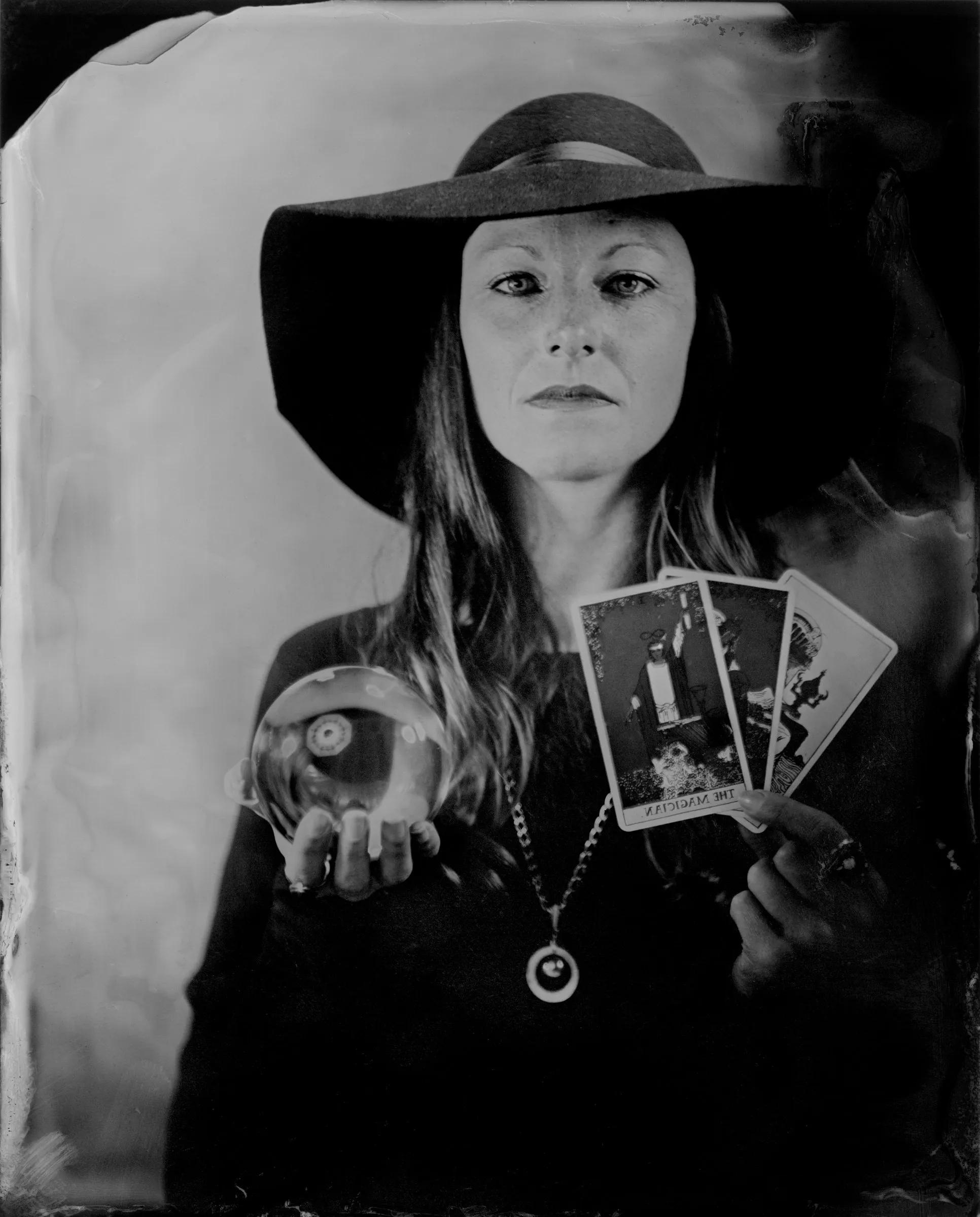 Vintage-style black and white portrait of Cora in a wide-brimmed hat, holding tarot cards and a crystal ball