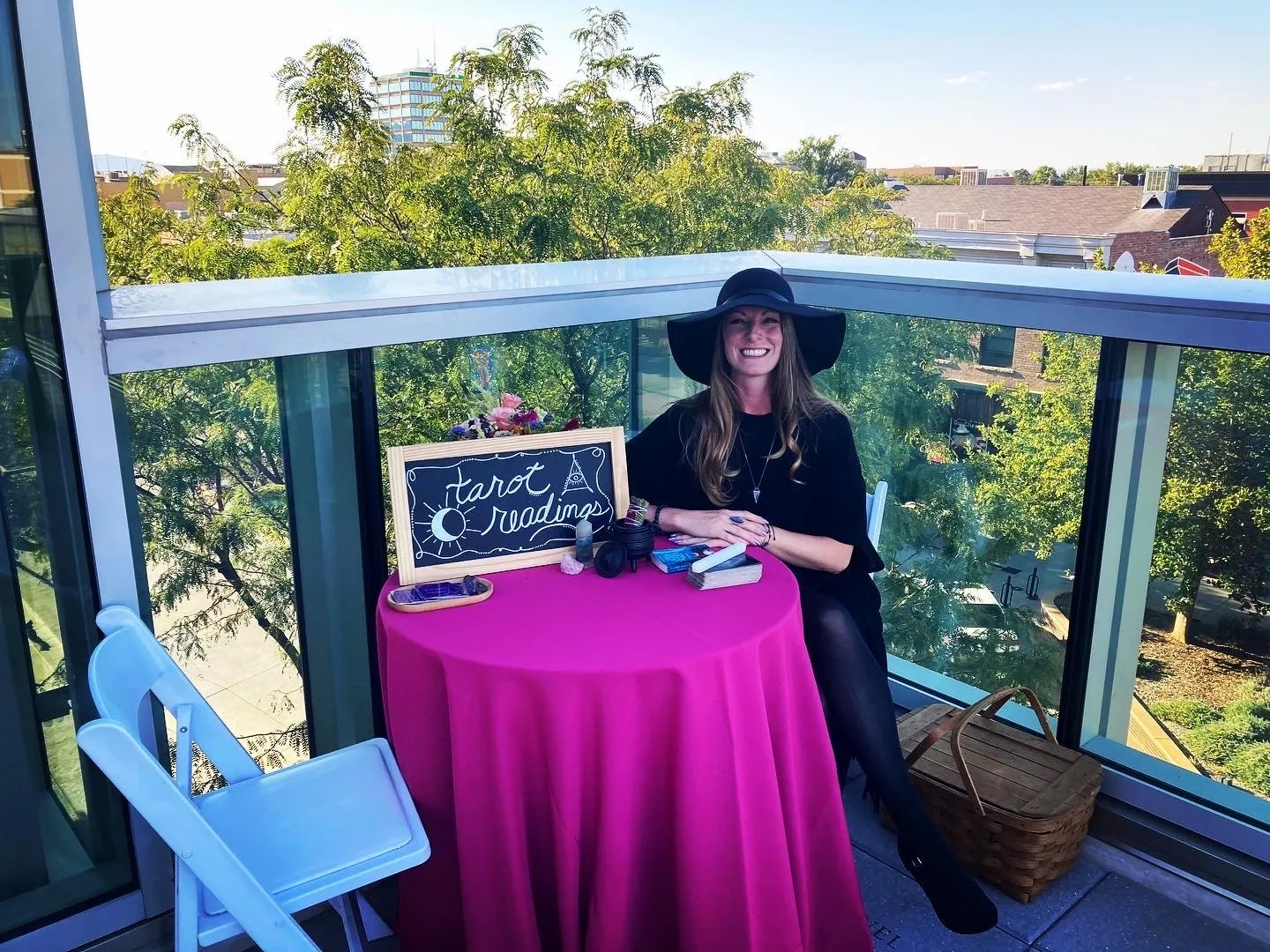 Cora giving tarot readings at a private rooftop event, seated at a table with a "Tarot Readings" chalkboard sign