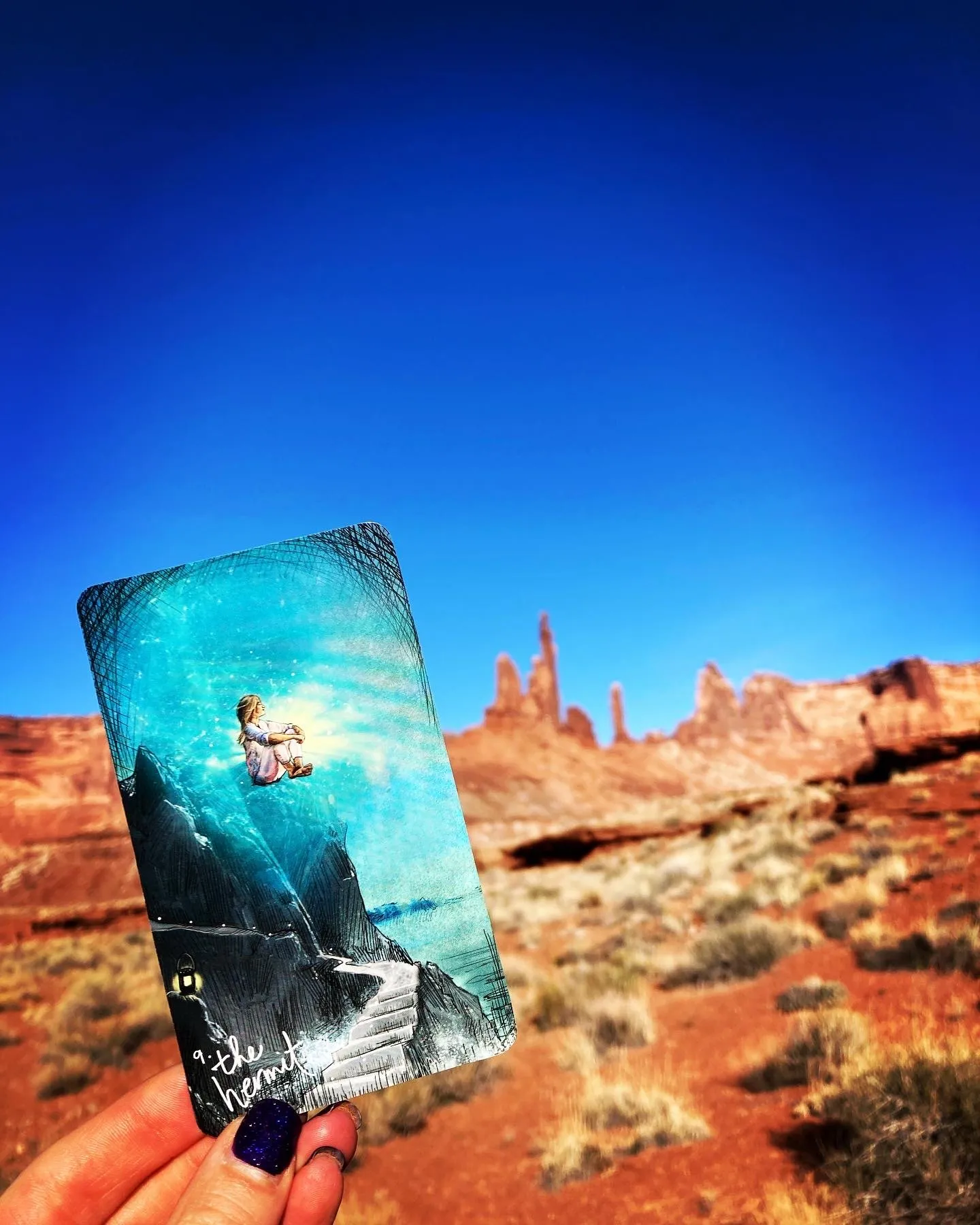 A tarot card held against red rock towers and deep blue sky