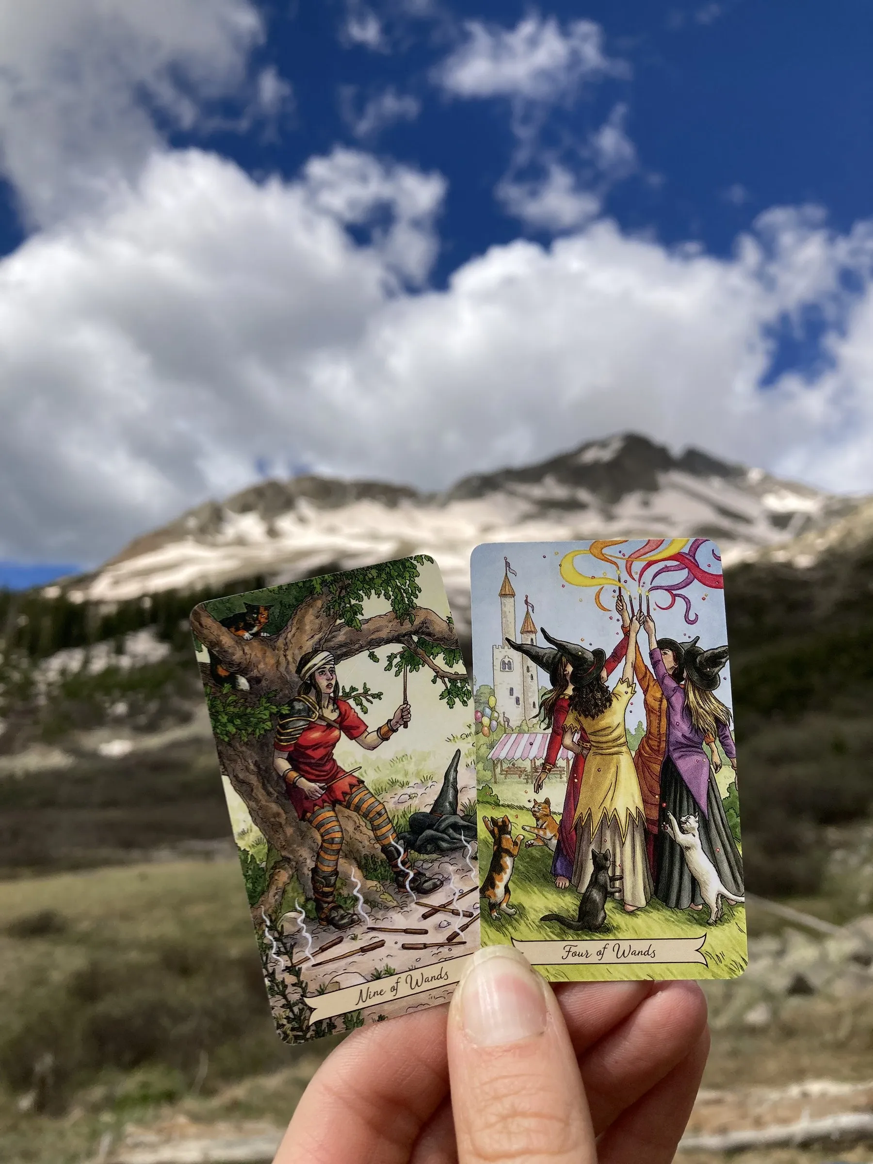 A tarot card held up against clouds and mountain sky