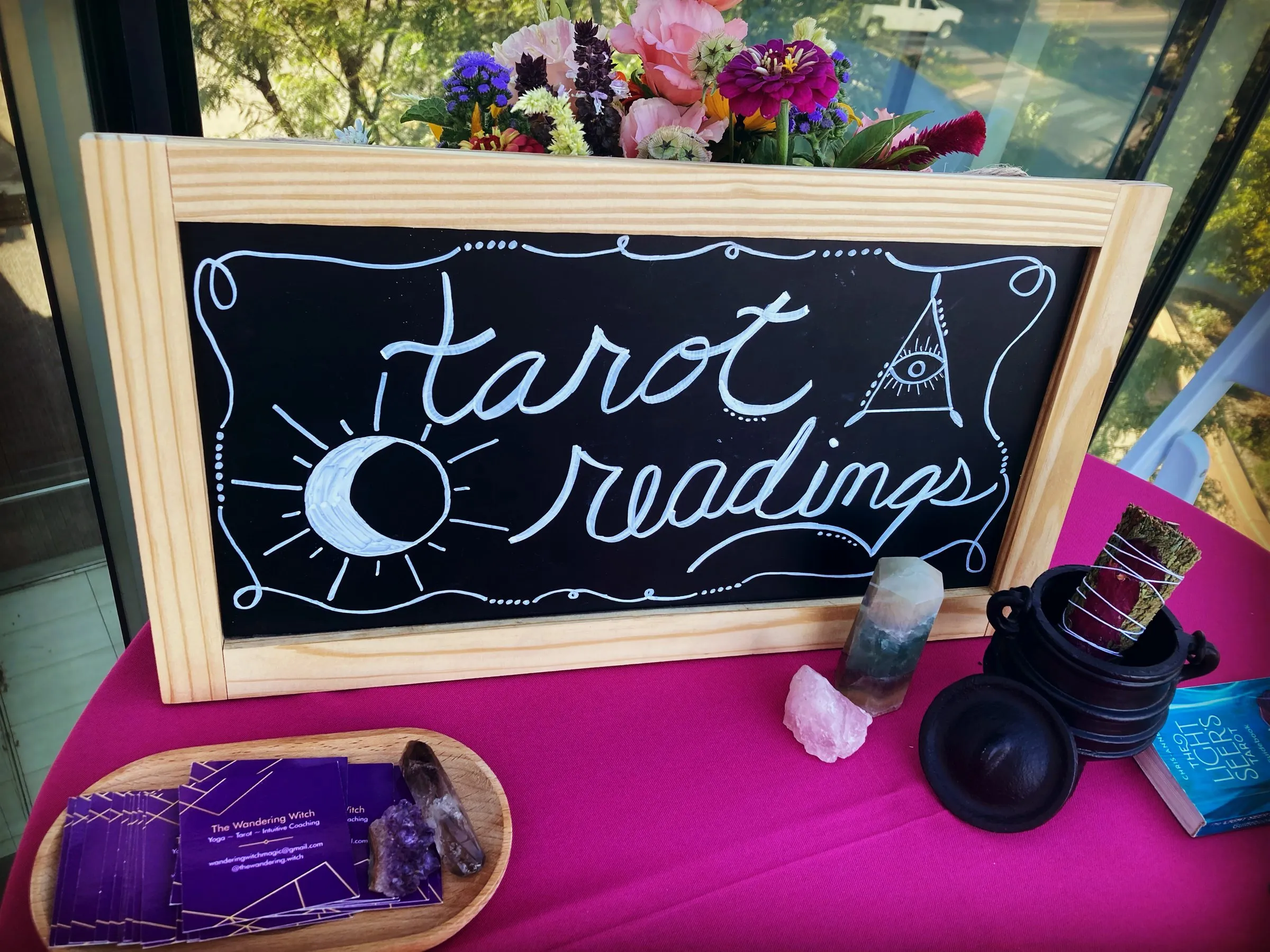 Cora's hand-lettered tarot readings chalkboard on a reading table with crystals