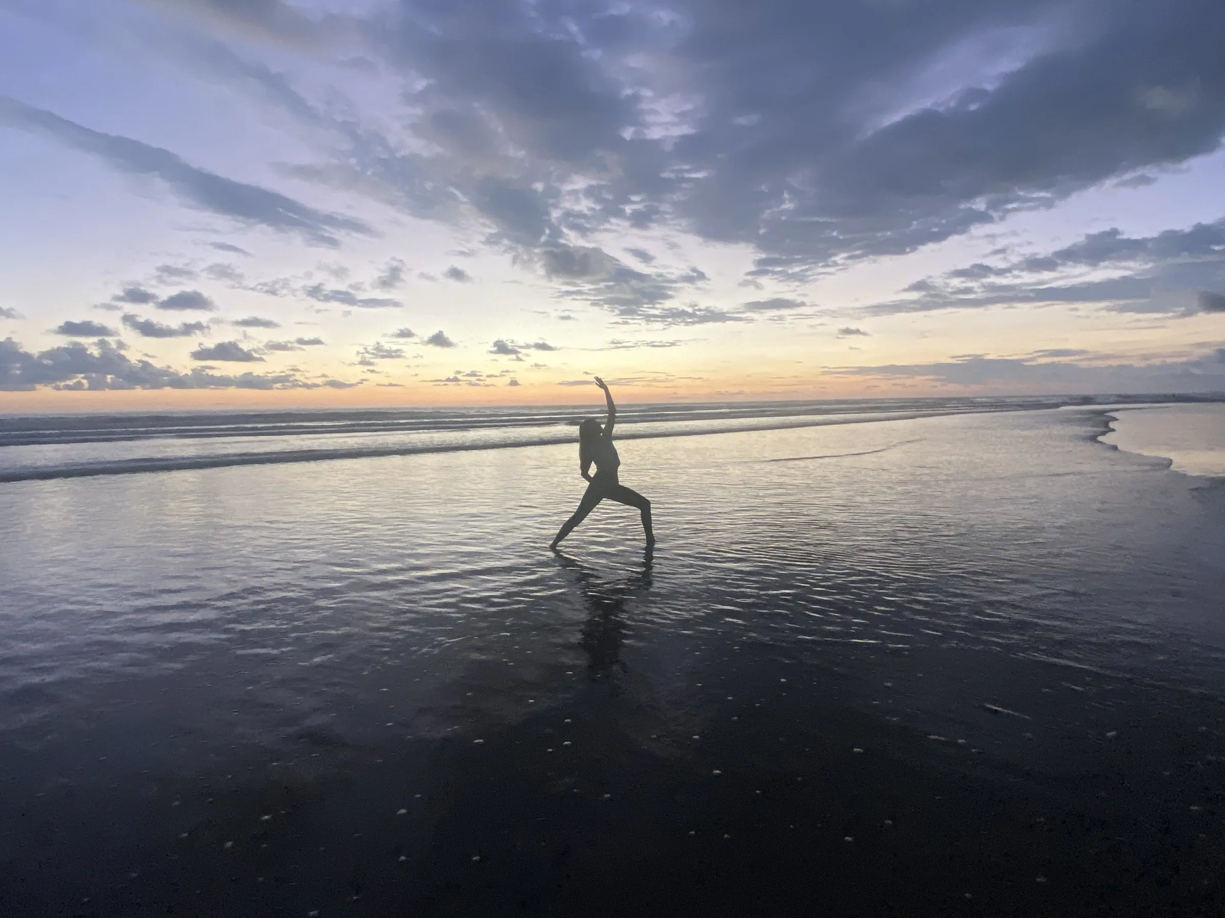 Cora holding a yoga pose on the beach at sunset, reflected in the wet sand