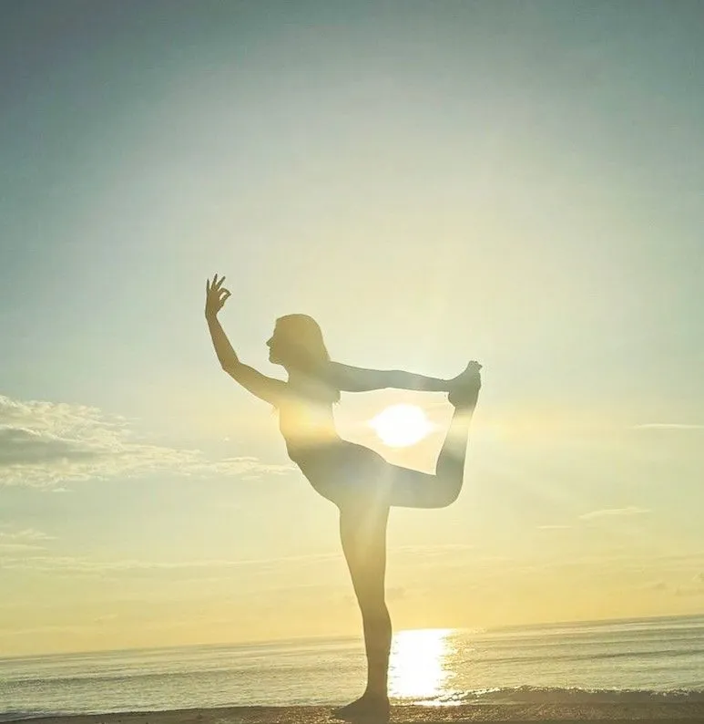 Cora in dancer's pose, silhouetted against an ocean sunset